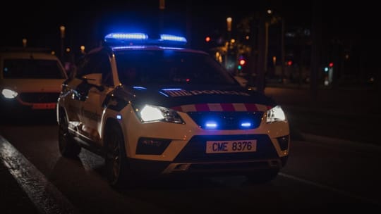 Police car with flashing lights on a Barcelona street at night, possibly during a pursuit or arrest.