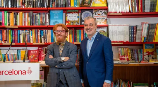 Mayor Jaume Collboni presenting the Barcelona bookstore support plan at a press conference, with books visible in the backgro
