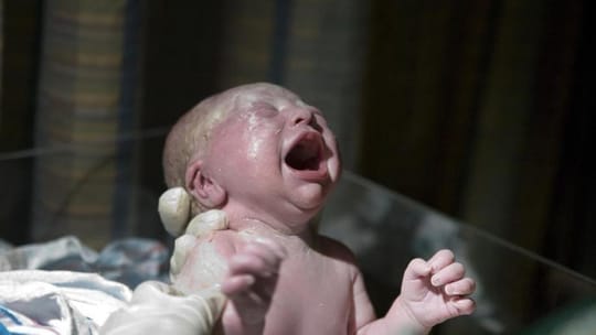 A midwife visiting a new mother and baby at home, showing a supportive postpartum care scene.