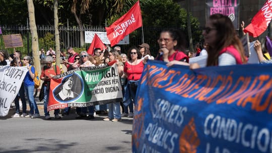 A large group of Barcelona municipal workers marching through a city street, holding protest signs and banners.