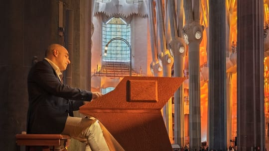 A close-up of an organ's multiple keyboards and pedalboard, showing the intricate controls and pipes in a dimly lit church in