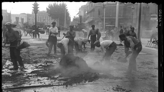 Historic black and white photo of workers paving Rambla de Catalunya near Gran Via in 1928, with old buildings in the backgro