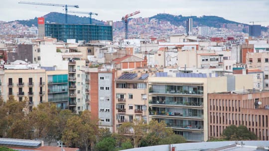 A 'For Rent' sign displayed in a window in Barcelona, with a blurred street scene in the background, symbolising the city's r