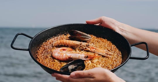 A vibrant outdoor dining terrace overlooking the Mediterranean Sea in Barcelona, with people enjoying rice dishes.