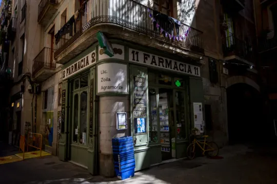 Exterior view of Farmàcia Agramonte, a historic Barcelona pharmacy with green wooden doors and engraved glass windows.