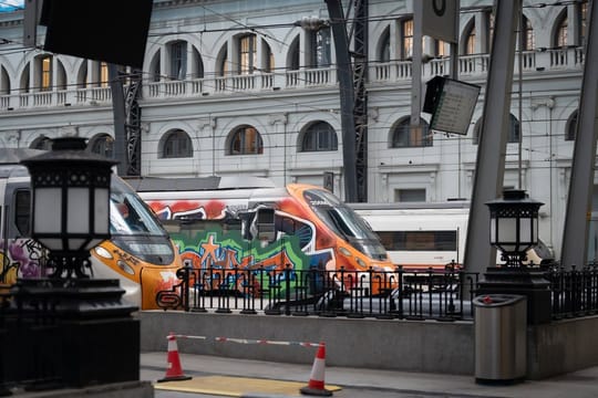 A Rodalies train on tracks with green vegetation in the background under a clear sky.