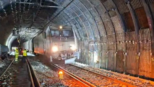 A freight train travelling through a tunnel, with visible reinforcement structures on the tunnel walls.