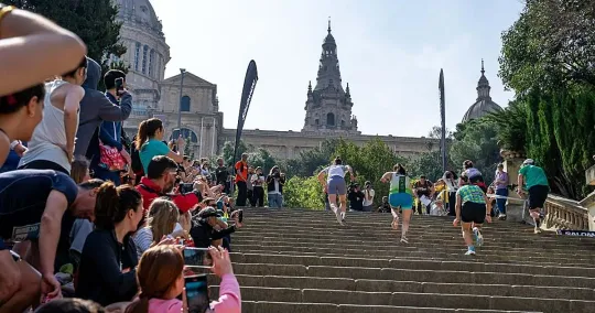 Runners ascend a steep staircase on Montjuïc mountain with Barcelona city views in the background during the Salomon Run.