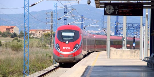 An Iryo high-speed train at a station platform, with passengers boarding or disembarking.