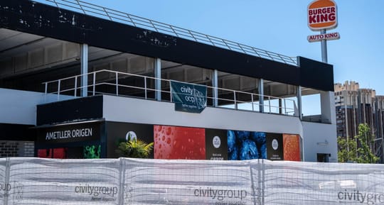 Exterior view of a modern Ametller Origen supermarket with fresh produce displays visible through large windows.