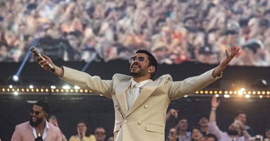 Bad Bunny performing on a minimalist stage with a large panoramic screen at Estadi Olímpic Lluís Companys, surrounded by a ma