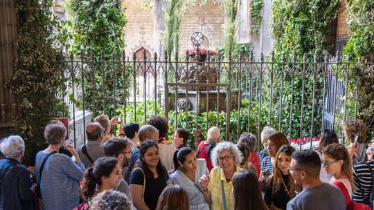 An 'ou com balla' installation with an egg spinning on a water jet in a historic Barcelona cloister, surrounded by flowers.