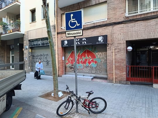 A blue parking sign in Barcelona with the word "MINUSVÀLID" in white capital letters, indicating a parking space for disabled