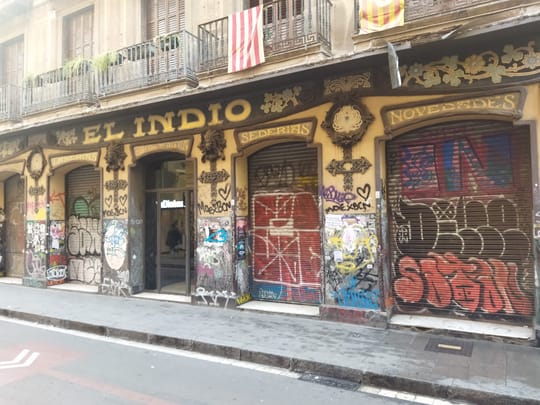 The neglected facade of El Indio shop on Carrer del Carme in Barcelona's Raval district, covered in graffiti.