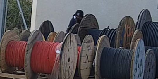Police officers in uniform inspecting a pile of scrap metal, possibly copper or aluminium, at an industrial site.