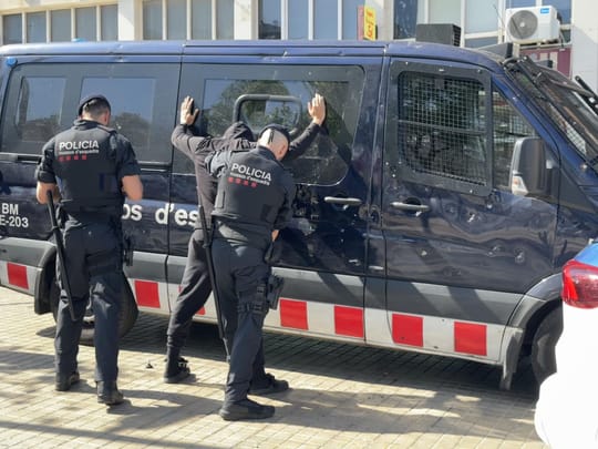 Mossos d'Esquadra officers on patrol in a busy Barcelona street, with historic buildings in the background.