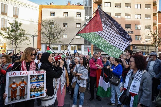 Protesters waving Palestinian flags and holding banners during a demonstration in Barcelona, with police in the background.