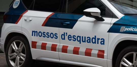 A Mossos d'Esquadra police car parked near a school building in Barcelona, with students visible in the background.
