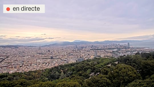 Dark clouds gather over Barcelona city, with rain starting to fall over buildings and the sea in the distance.