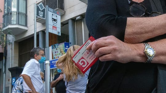 A person holding a pink public transport card, possibly the Tarjeta Rosa, at a Barcelona Metro station ticket barrier.