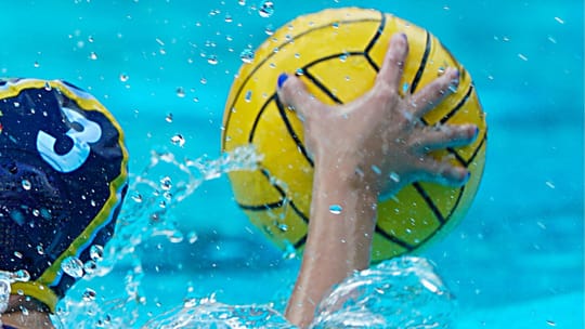 Women's water polo players in action during a match, with two teams competing in a pool.