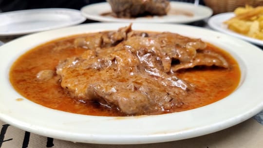 A plate of orange-copper fricandó with veal, mushrooms, and a rich sauce, served at Casa Ana in Poblenou, Barcelona.