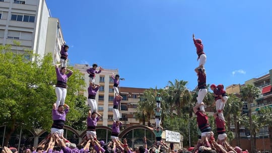 A human tower (castell) with many people in traditional white trousers and sashes, reaching several levels high, with a crowd