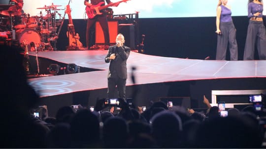 Eros Ramazzotti performing live on stage at Palau Sant Jordi, holding a microphone.