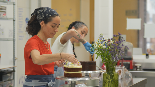 Two Chilean sisters, Claudia and Constanza Bravo, smiling in their pastry shop Rayün, surrounded by beautifully decorated glu