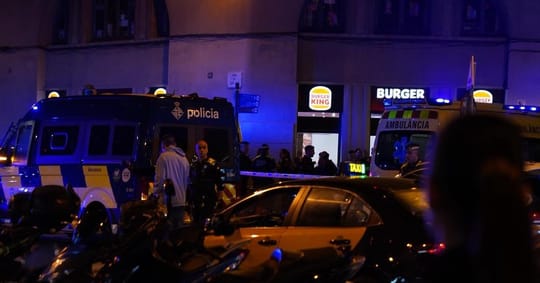 Police tape and emergency services vehicles at a crime scene in a Barcelona street at night.