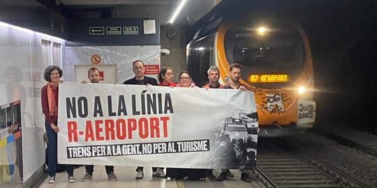 People gathered at Passeig de Gràcia Rodalies station platform in Barcelona, holding banners about public transport.
