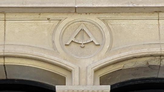 A close-up of a building facade in Sarrià, Barcelona, showing a carved compass and level symbol above a window.