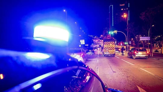 Mossos d'Esquadra and Guardia Urbana police vehicles patrolling a street in Barcelona at night.