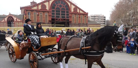 Horses and carriages parading through a city street during the Tres Tombs de Sant Antoni festival in Barcelona.