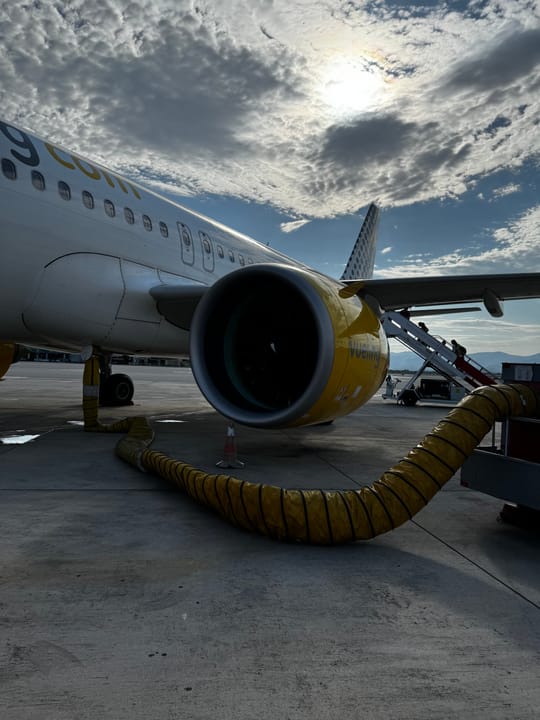 A Vueling plane on the airport tarmac with passengers boarding by mobile steps under a cloudy sky.