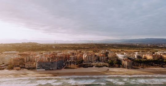 People celebrating Sant Joan on a beach at night, with bonfires and fireworks in the background.
