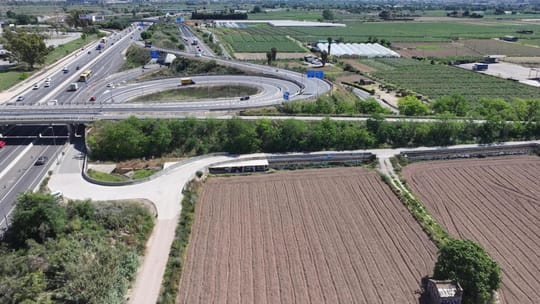 Aerial view of new motorway sections and junctions in the Baix Llobregat area, with cars driving on them, surrounded by green