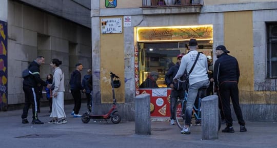 A diverse group of people walking through a busy street in Barcelona's Ciutat Vella district, with historic buildings in the 