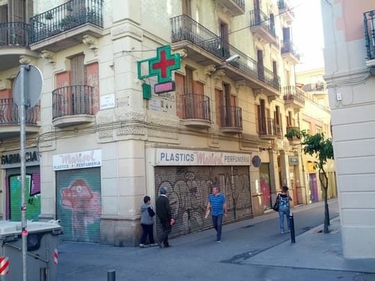 Illuminated green pharmacy cross above a farmacia on a Barcelona street corner
