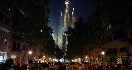 The illuminated Jesus Christ Tower of Sagrada Família with a large cross on top, against a night sky.