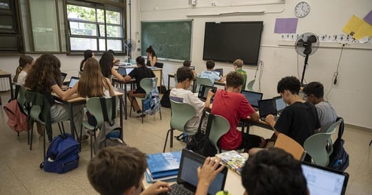 Students in a classroom looking uncomfortable due to high temperatures, with a digital thermometer displaying over 30°C.