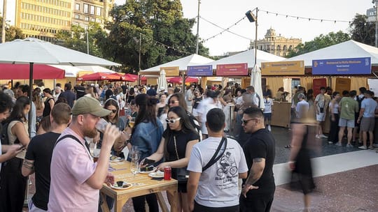 People enjoying food and drinks at outdoor stalls in Plaça Catalunya, Barcelona, during a gastronomic fair.