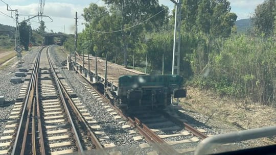 A Rodalies train carriage on tracks, with a blurred background of a station or railway line.