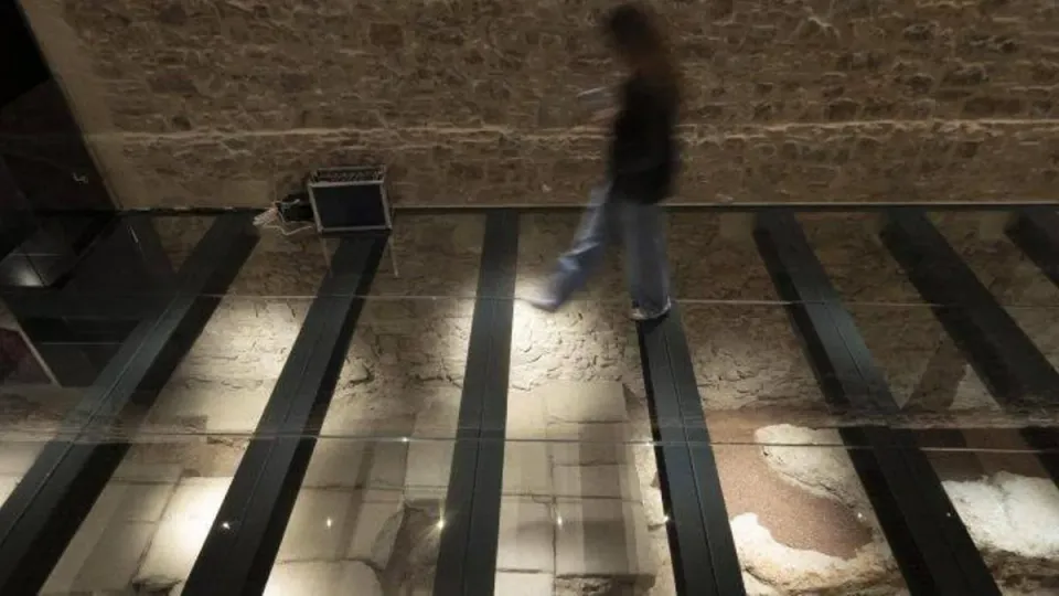 Archaeologists examining ancient Roman paving stones in an excavation site in Barcelona, with historic buildings in the backg