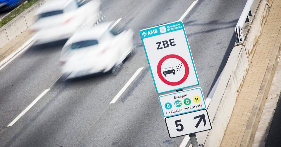 A yellow-label car driving through a low-emission zone in Barcelona with a sign indicating restrictions.