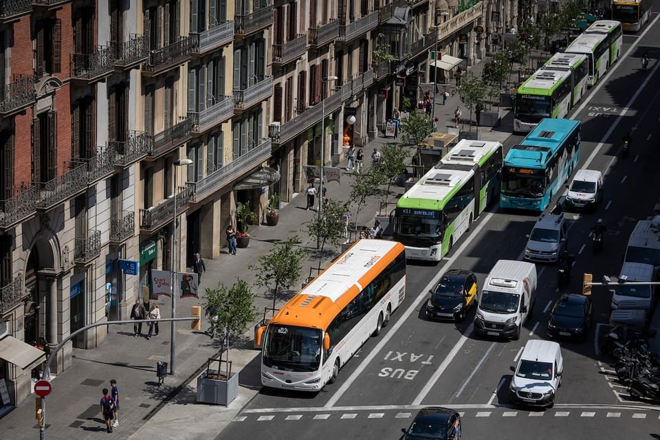 Intercity buses parked along a busy street in Barcelona's city centre, with pedestrians walking on the pavement and historic 