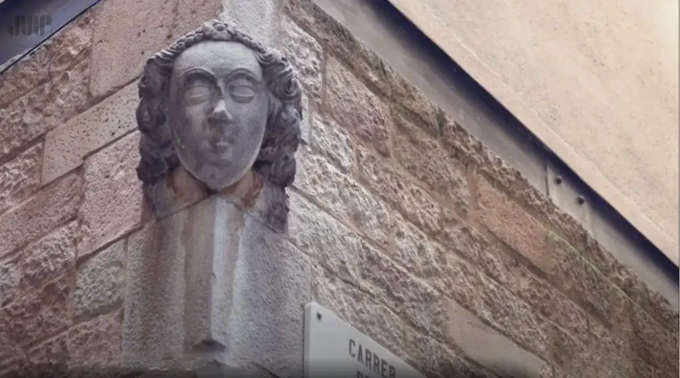 A carved stone grotesque face, or 'carassa', embedded in an old building wall in Barcelona's Ciutat Vella district.