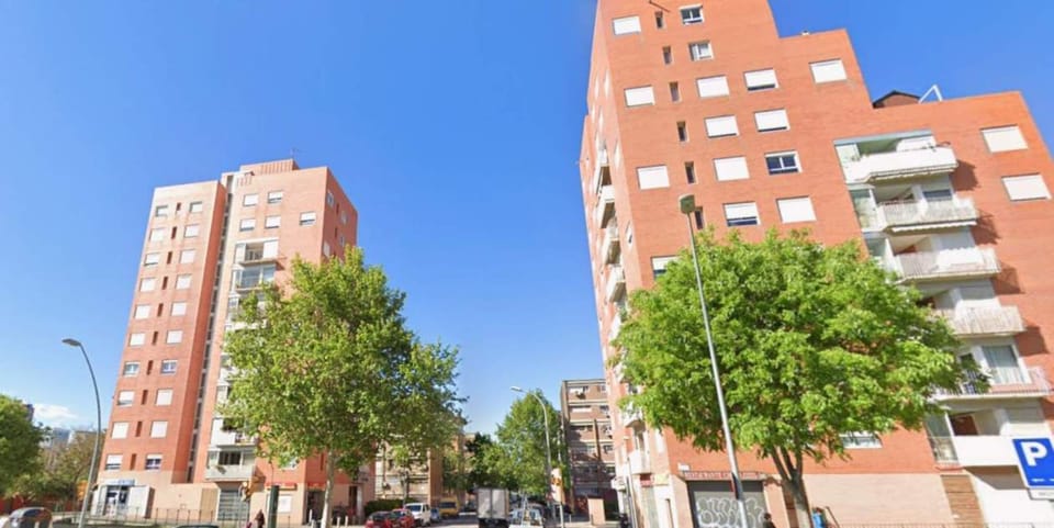 Police officers conducting a raid on a building, with a police vehicle visible, in a residential street in Barcelona.