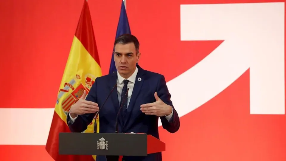 Spanish Prime Minister Pedro Sánchez speaking at a podium with a Spanish flag in the background.