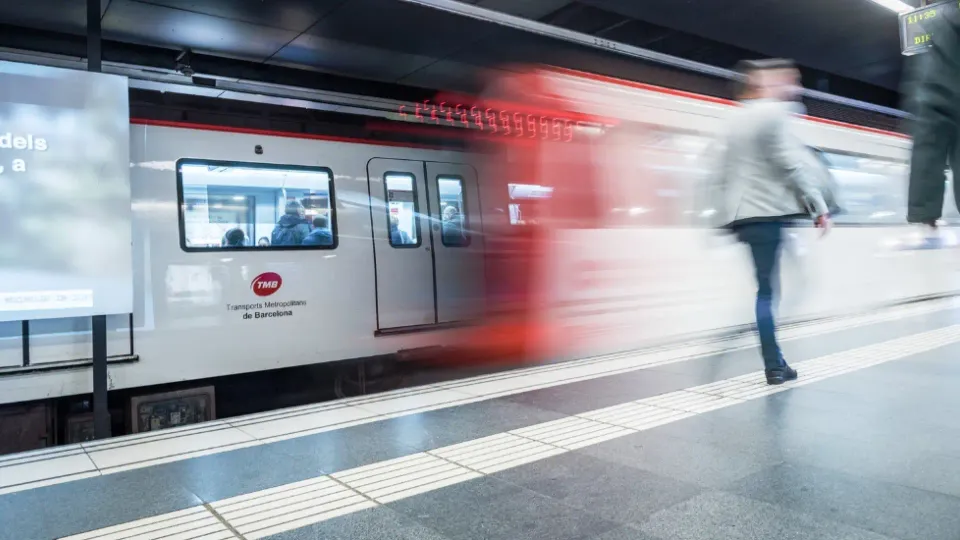 A modern Barcelona Metro train arriving at a station platform, with passengers waiting.